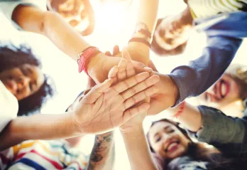 A variety of adults smiling and all putting their hands in a circle