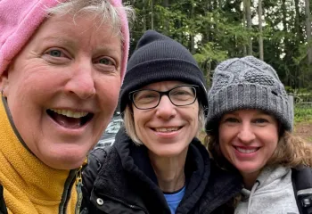 3 women in knit hats smiling about their hike