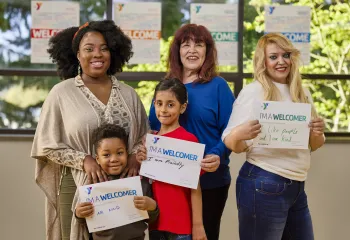 A diverse group of people of different ages holding up signs explaining how they are welcomers.