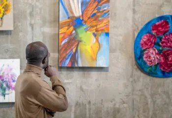 A man looking contemplatively at a gallery wall of paintings.