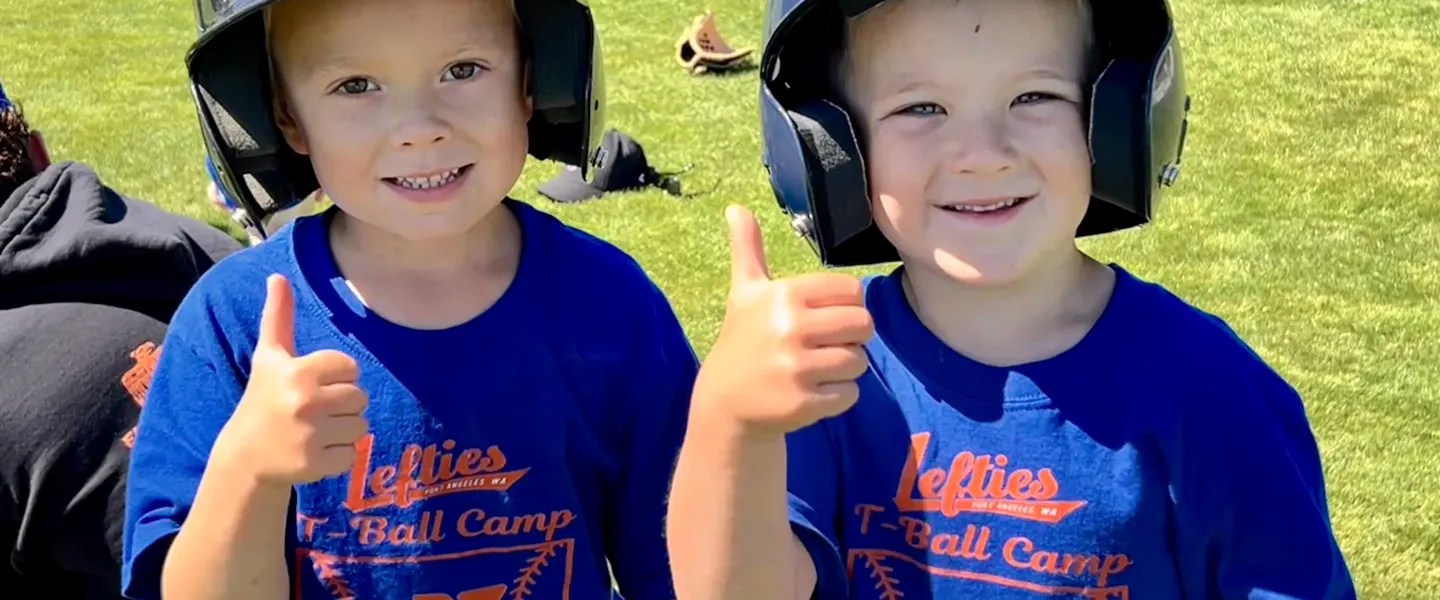 Two youth with t-ball gear on giving a thumbs up to the camera