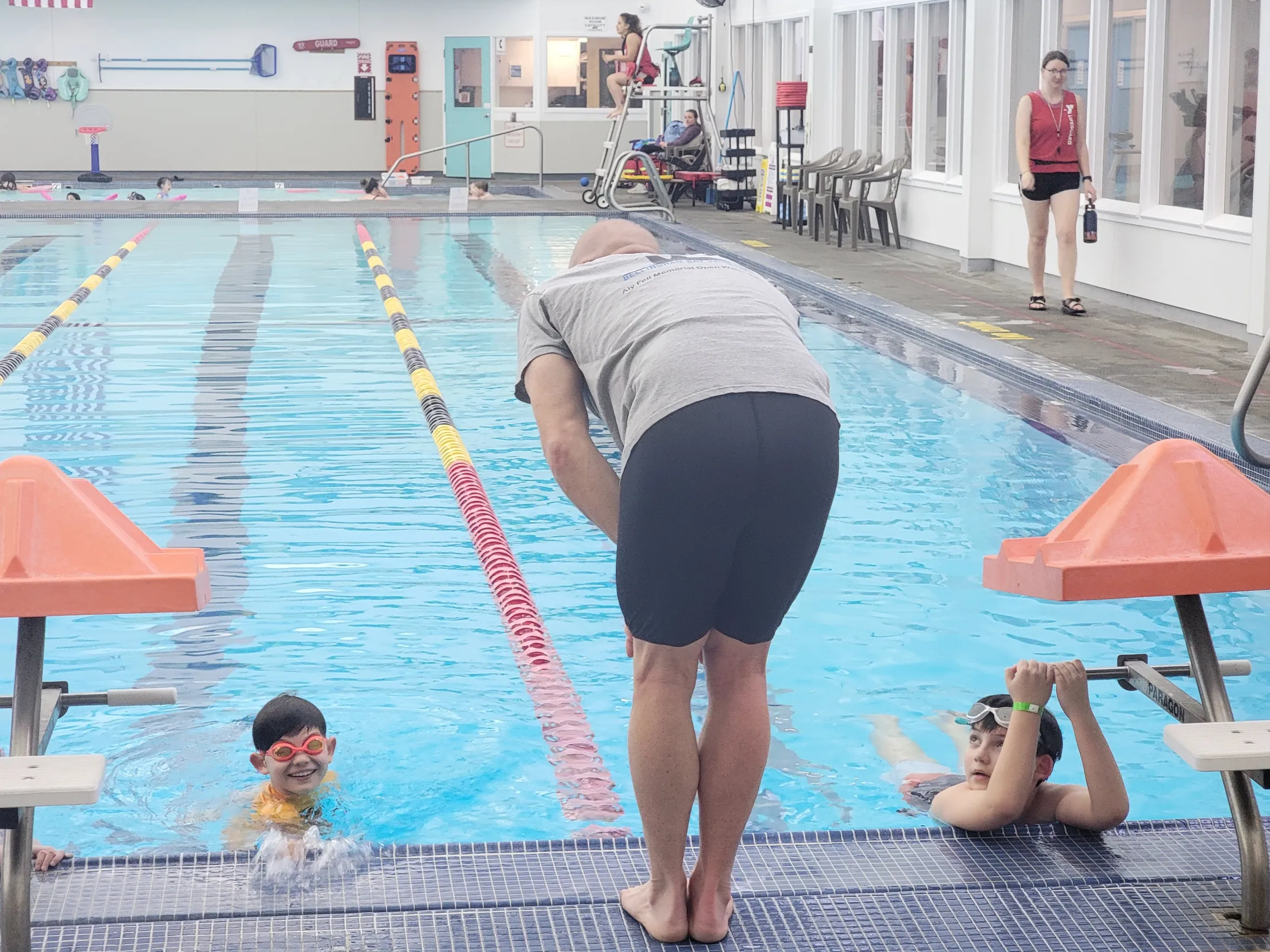 Adult bending over a pool talking to two kids in the pool