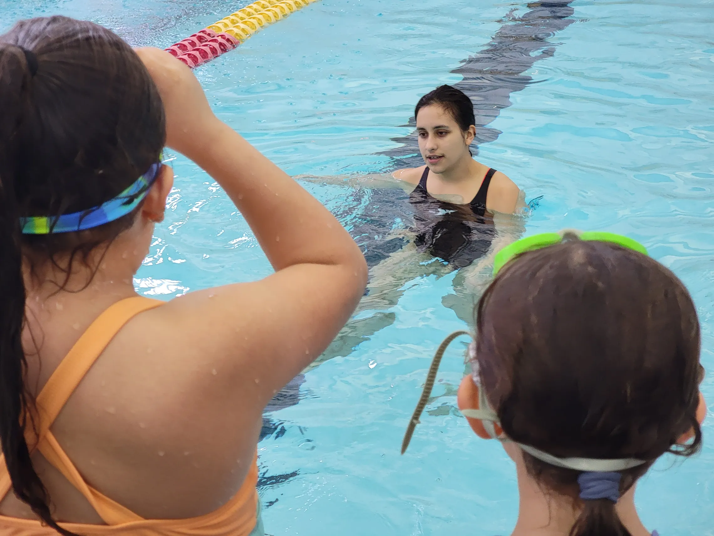 Woman in a pool teaching kids sitting on the side of the pool