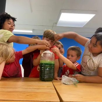 kids in a circle at a table around a science experiment