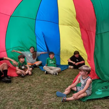 children sitting under a parachute