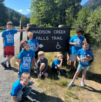 A group of camp kids standing outside next to a Madison Falls sign