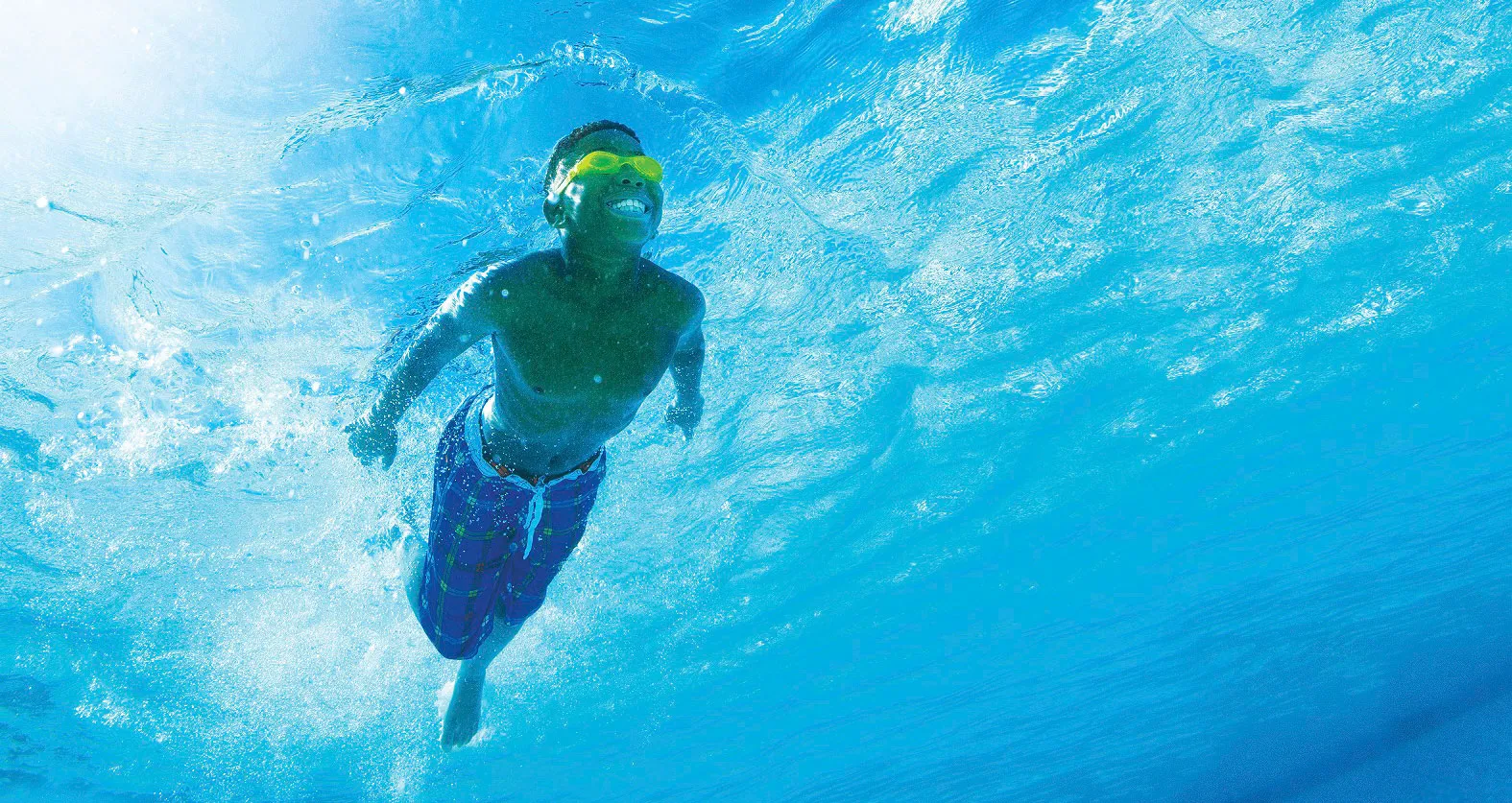 black child swimming with goggles on view from under the water