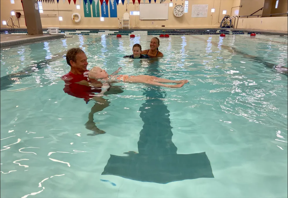Swim instructor in the water with a young child floating on their back during swim lessons