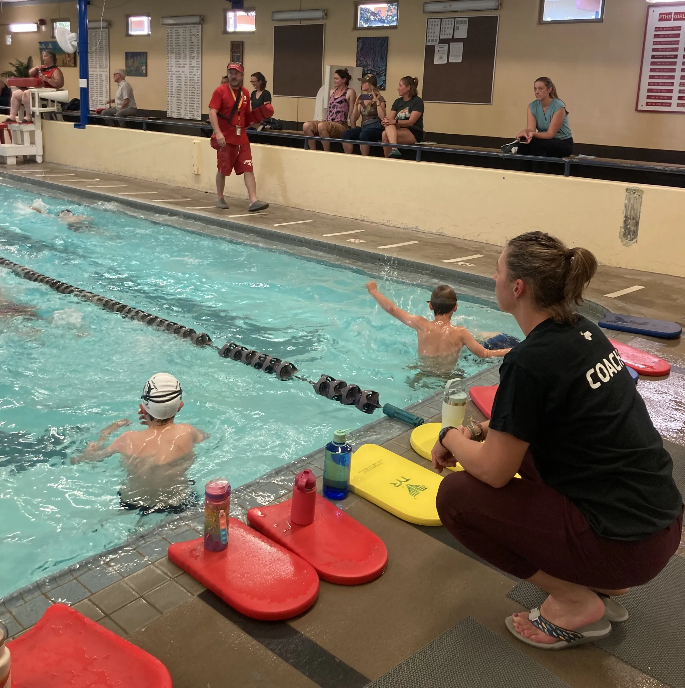 Coach on the side of the pool with swim league participants in the pool.