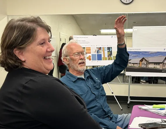Professional woman and man sitting in a board meeting with the man's hand raised