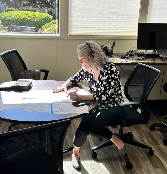 woman sitting at a desk writing a grant with sunlight streaming through the window