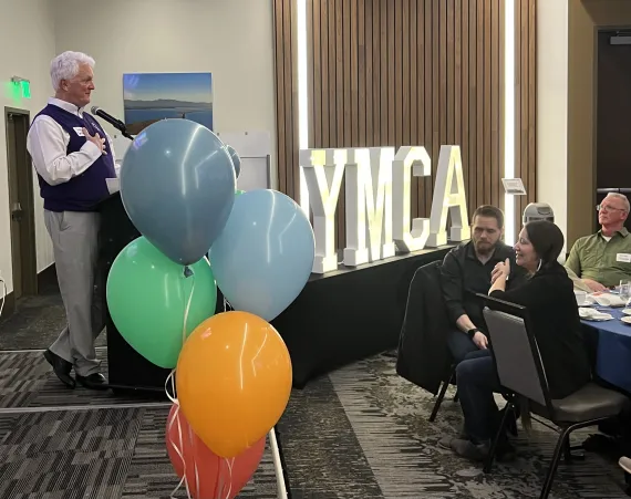 A gentleman on a stage with balloons and YMCA marquis letters