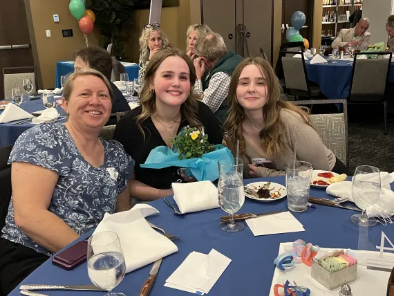 A woman and two teen girls sitting at an event table.