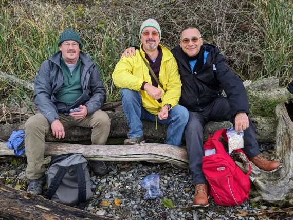 Three men resting on a log after a group hike.