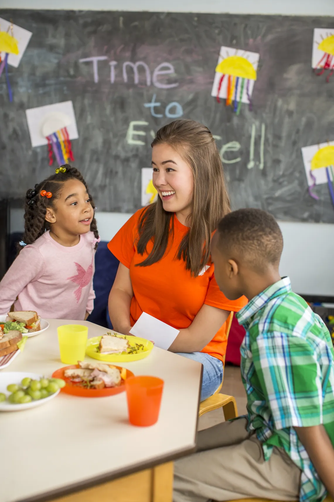 A Woman in a classroom setting laughing with children.