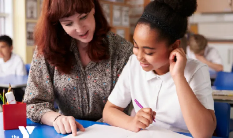 A photo of an adult woman helping a young lady at school