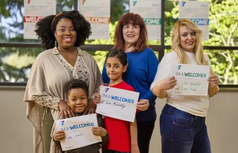 A diverse group of people of different ages holding up signs explaining how they are welcomers.
