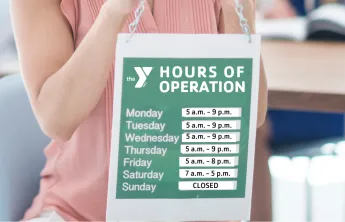Woman holding up a sign with hours of operation for YMCA branch hours
