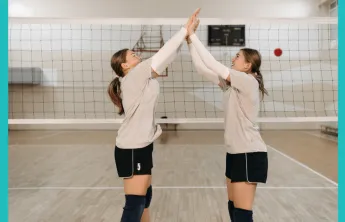 Image of two teen ladies high fiving near a volleyball net