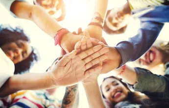 A variety of adults smiling and all putting their hands in a circle
