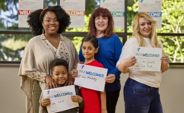 A diverse group of people of different ages holding up signs explaining how they are welcomers.