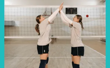 Image of two teen ladies high fiving near a volleyball net