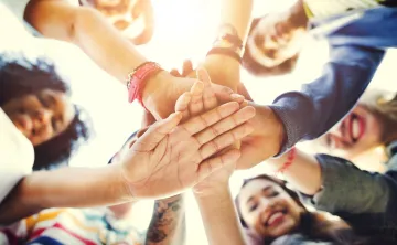 A variety of adults smiling and all putting their hands in a circle